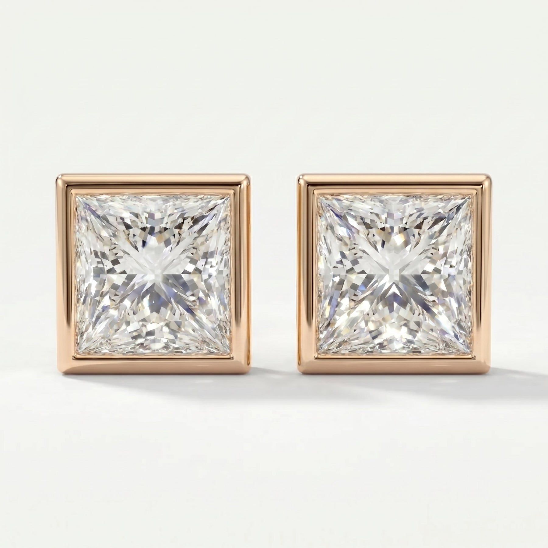 Pair of square-cut diamond earrings with rose gold settings on a white background