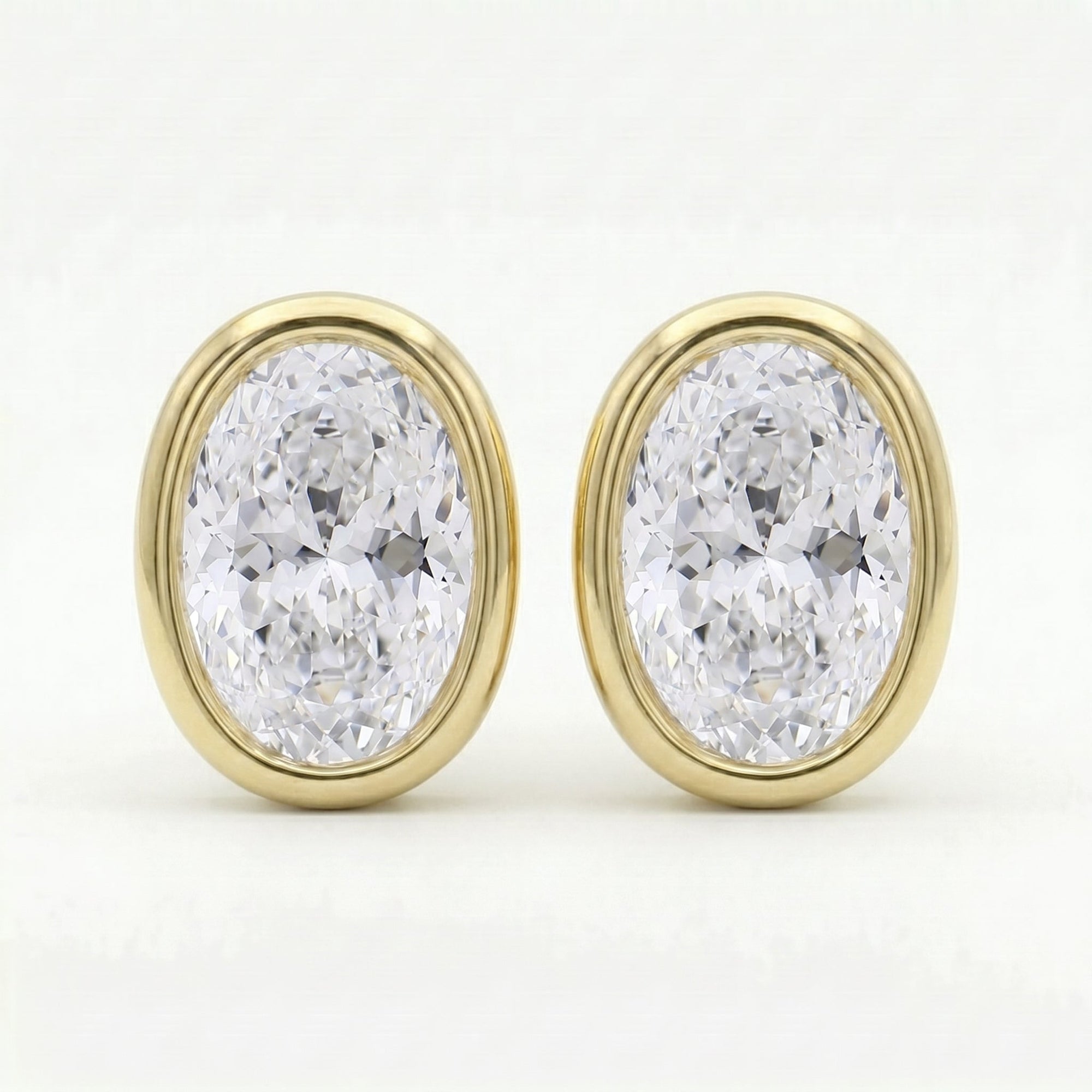 Oval bezel-set diamond stud earrings in polished yellow gold with brilliant sparkle on clean white background