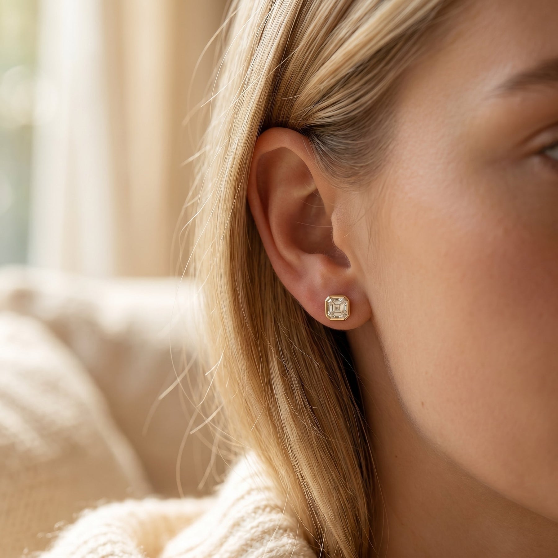Close-up of a person wearing a gold earring with a clear gemstone.