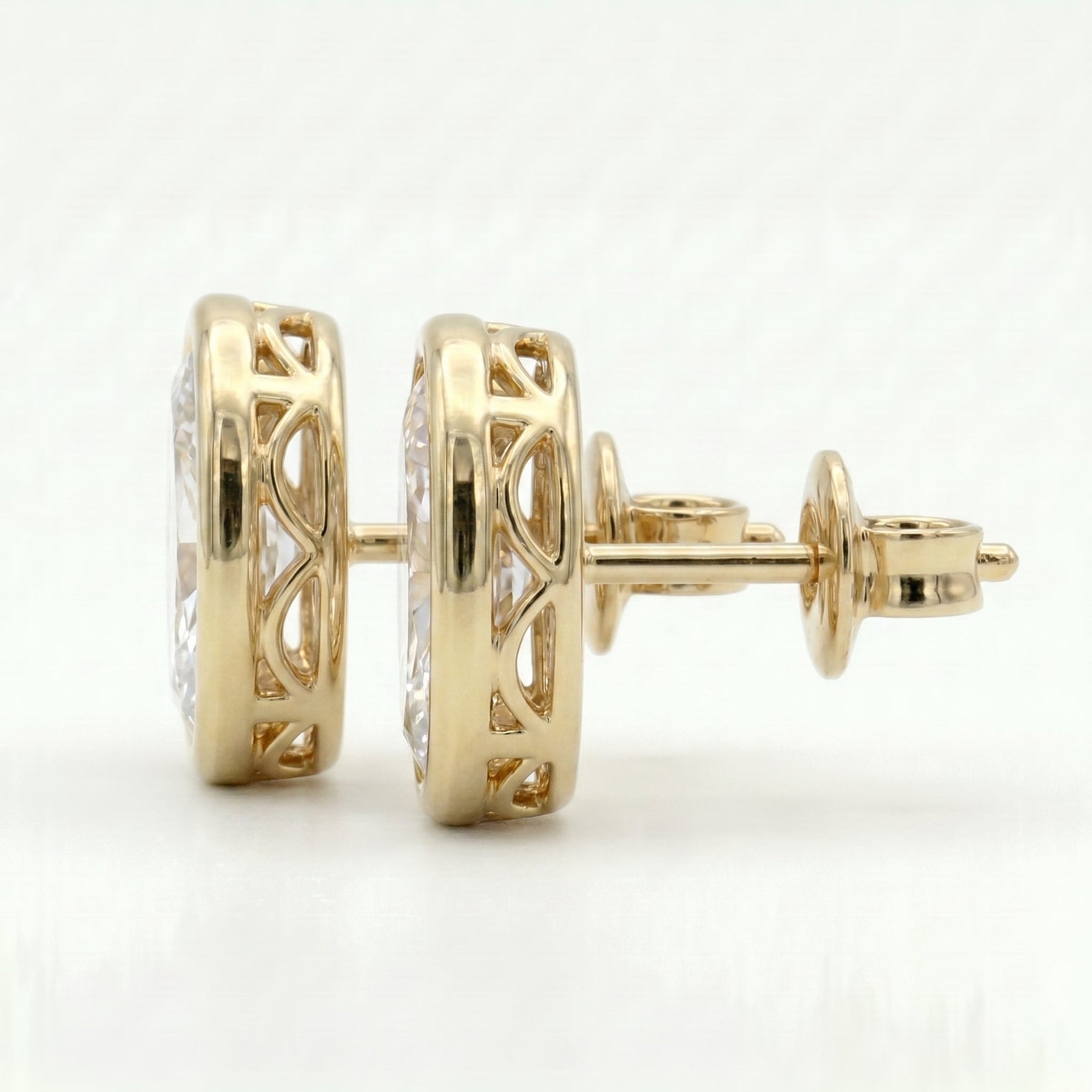 Side profile of oval diamond stud earrings showing open gallery bezel setting and gold craftsmanship