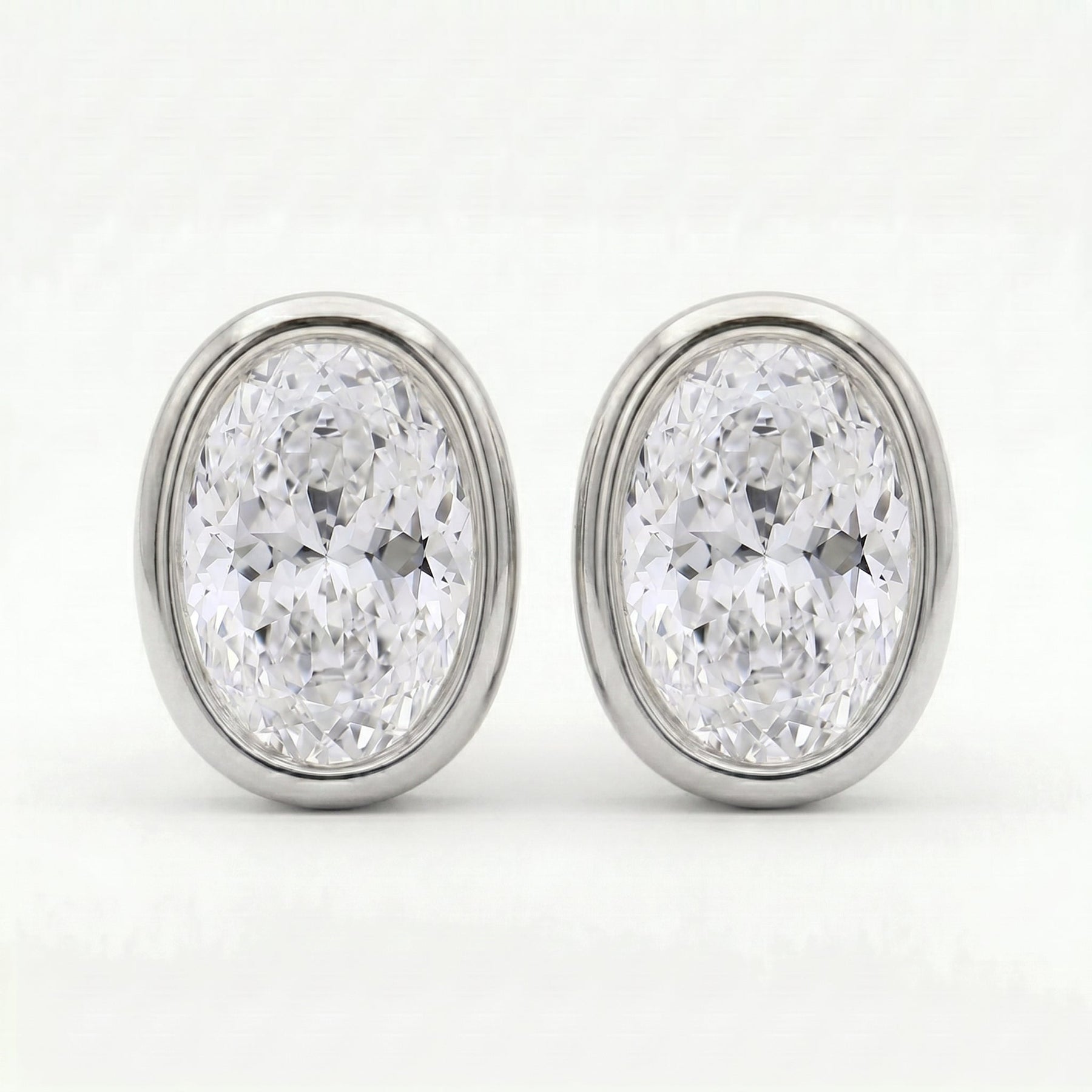 Luxury oval diamond bezel earrings angled view highlighting polished gold setting and brilliance