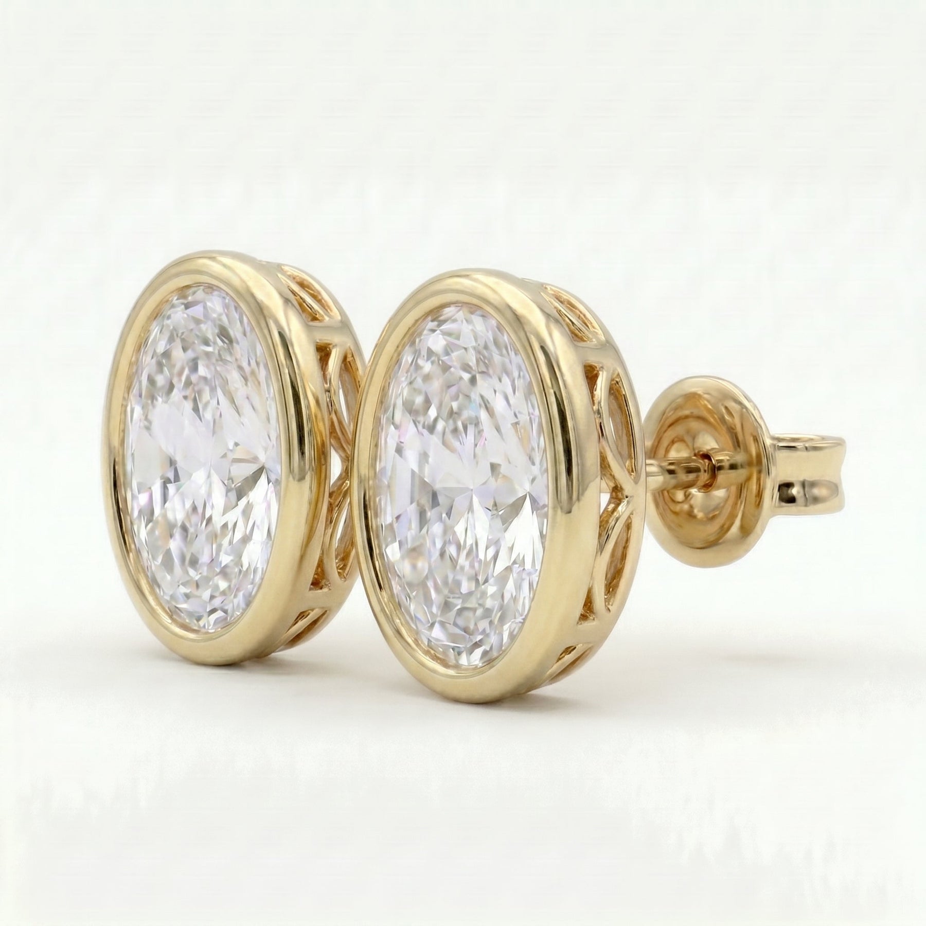 Yellow gold oval stud earrings with bezel setting shown at luxury 45-degree angle with high brilliance