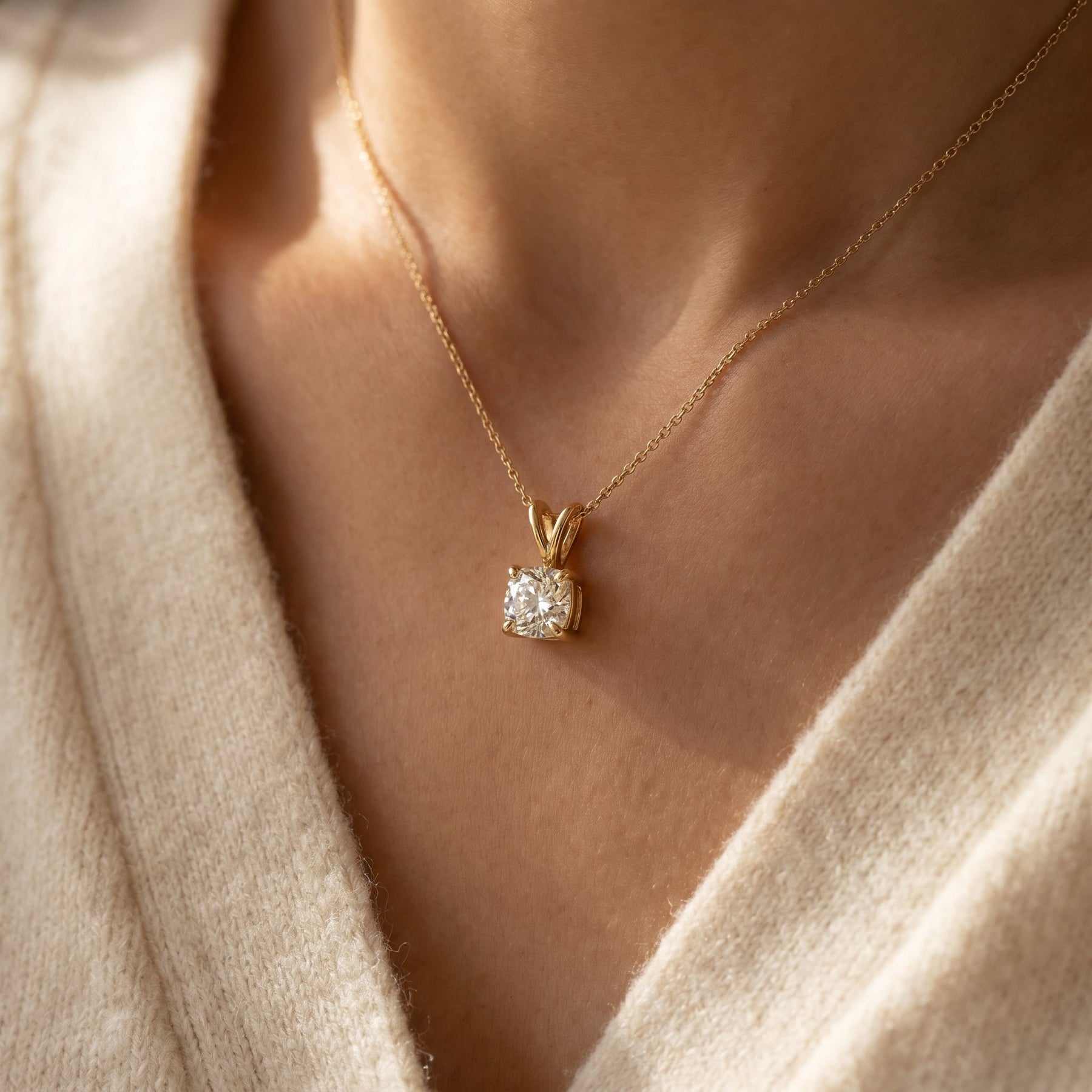 Gold necklace with a diamond pendant worn by a person in a beige sweater.