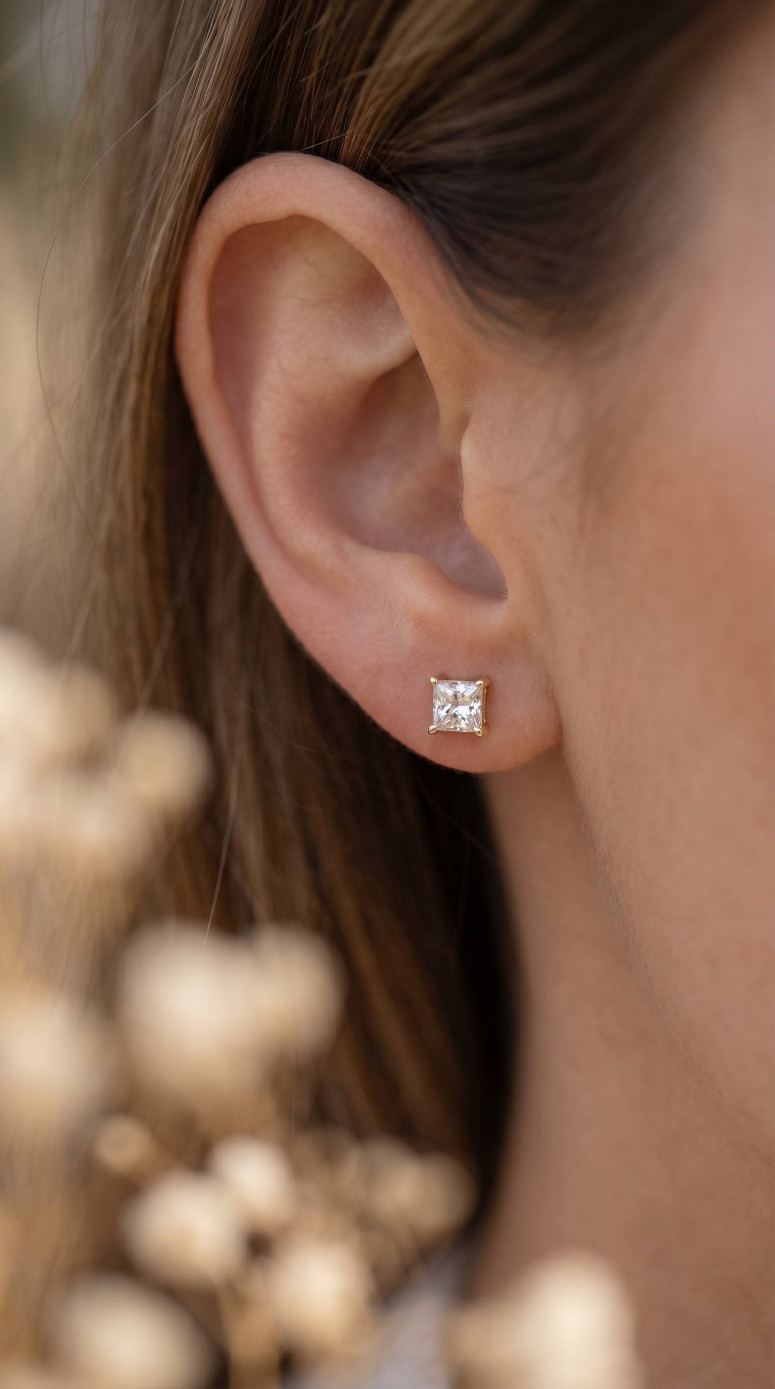 Close-up of an ear wearing a diamond stud earring with a blurred natural background