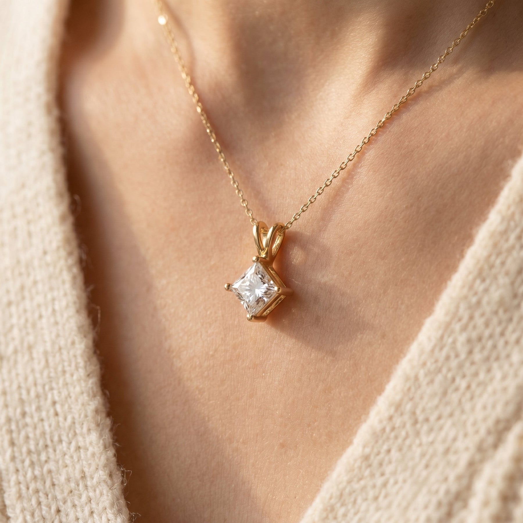 Gold necklace with a diamond pendant on a person wearing a beige sweater.