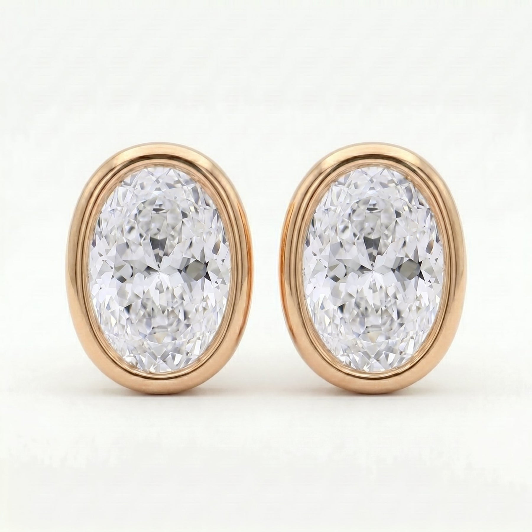 Oval diamond bezel stud earrings in rose gold with brilliant sparkle on clean white background